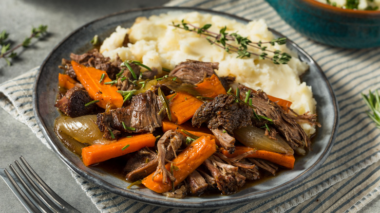 A pot roast is served on plate with mashed potatoes.