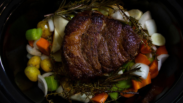 A whole seared pot roast sits in a slow cooker.