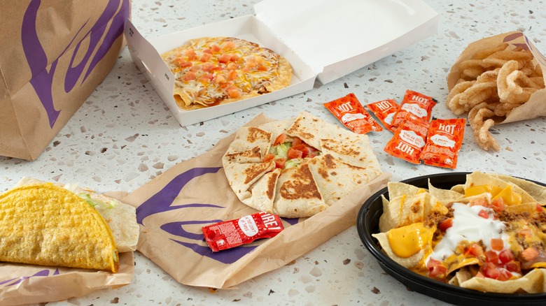 Taco Bell menu items including a crunchwrap, Mexican pizza, and nachos sit on a granite table