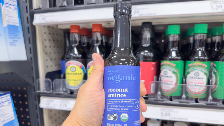 A hand holding a bottle of coconut aminos.