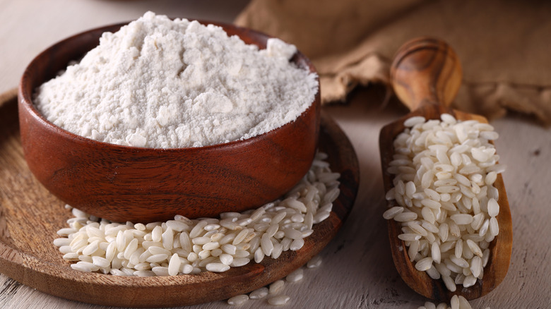 Rice flour in a wooden bowl alongside grains of rice