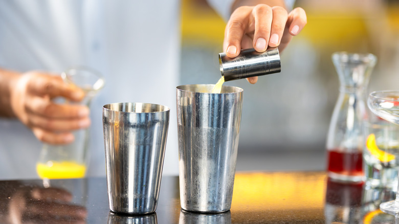 Person pours liquid from a measure into a silver cocktail shaker