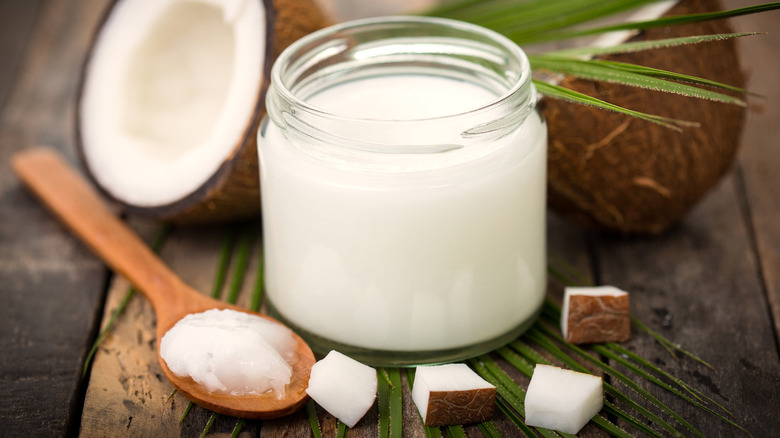 Coconut oil in glass jar with spoon and coconuts