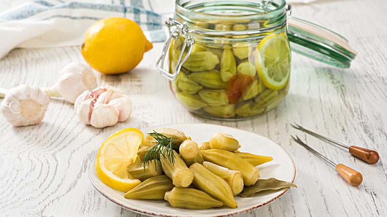 A plate of pickled okra sits next to a small jar of okra.