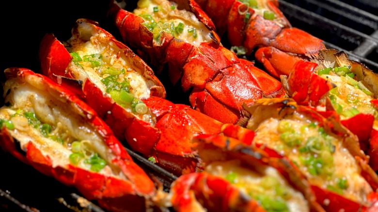 Two rows of lobster tails with green onions on the grill