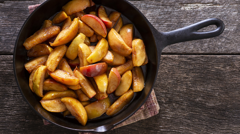 Cinnamon apple slices in a cast iron skillet on wood background