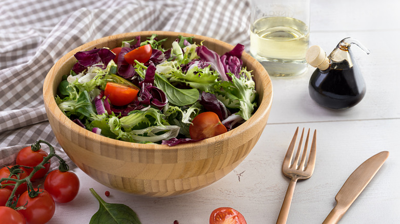 A bowl of green salad with tomatoes and various types of lettuce on a table