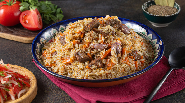 A bowl of rice pilaf on a burgundy napkin next to a spoon and various ingredients