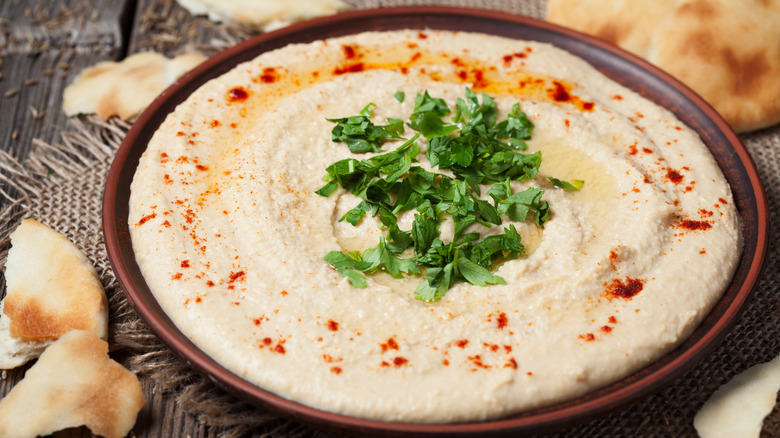 A bowl of hummus surrounded by bits of pita on a wooden table