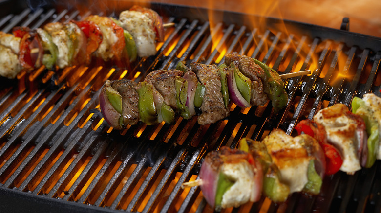 Two chicken kebabs and one beef skewer on a hot grill