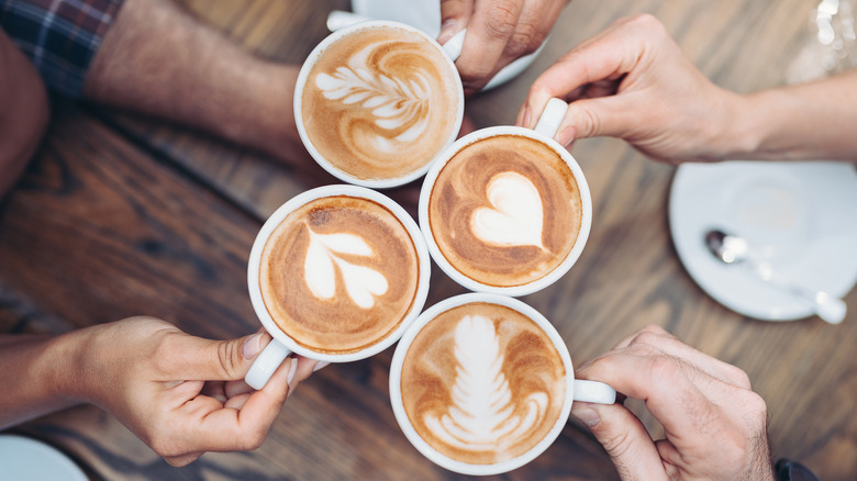 Various hands toasting cups of cappuccinos with foam art