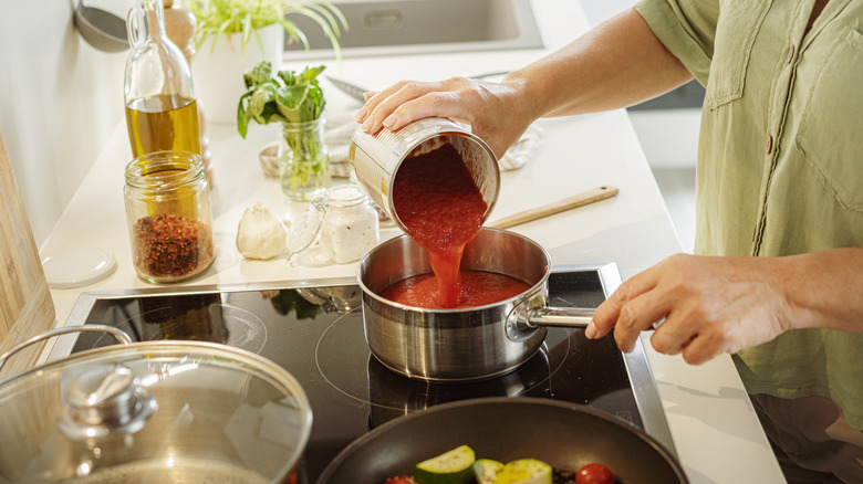 Person pours tomato puree into saucepan