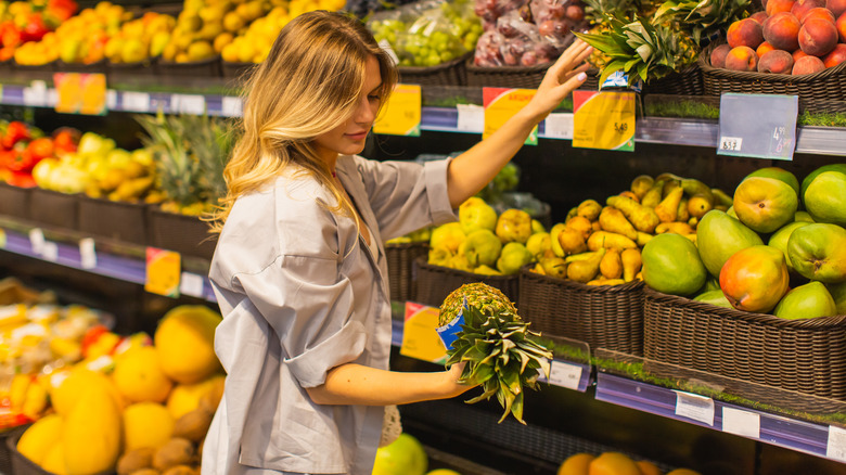 woman picking up pineapple in grocery store