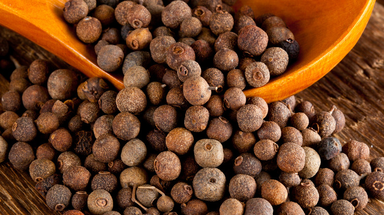 whole allspice in a spoon on a wooden table