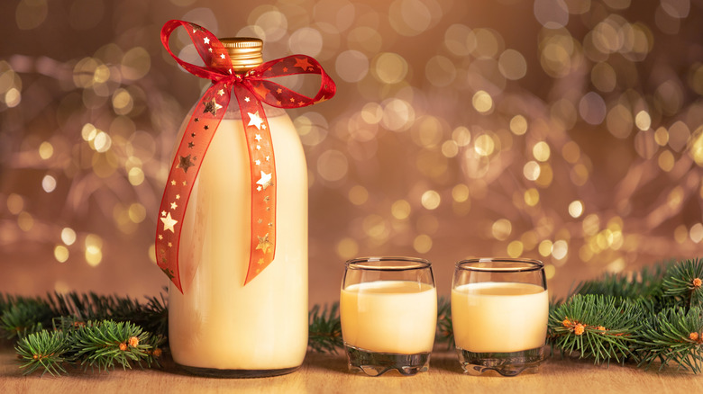 A bottle of homemade eggnog with a red ribbon with stars next to two glasses of eggnog and pine branches