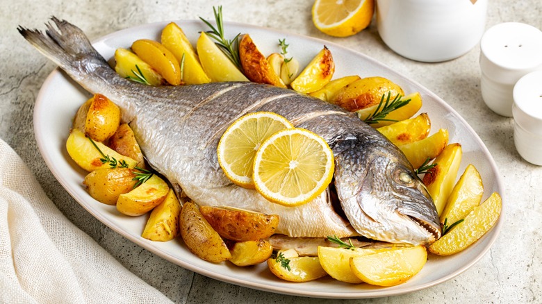 Whole orata on a plate of potatoes and rosemary, topped with lemon slices