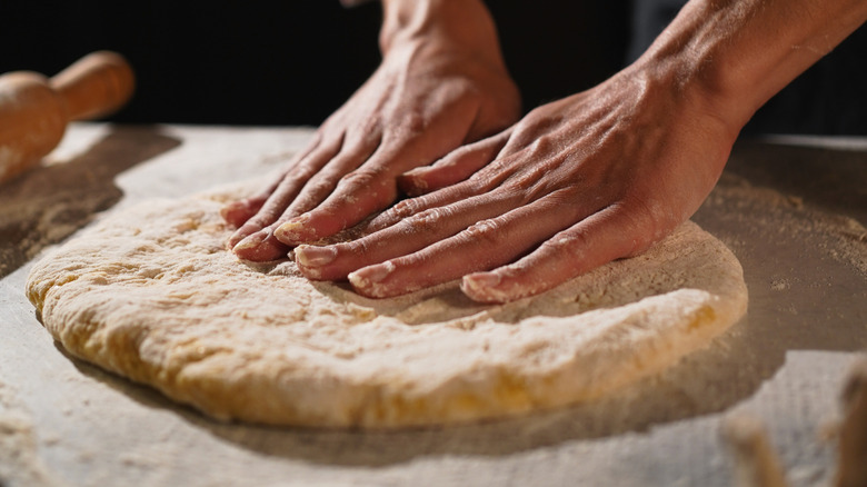 Hands forming raw pizza dough