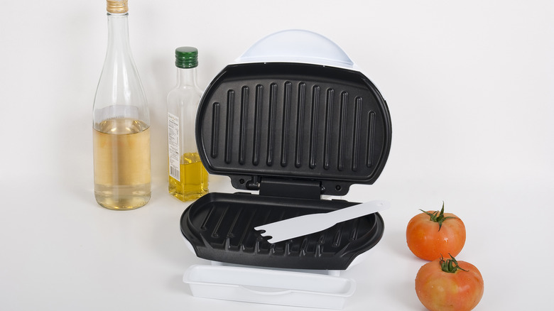 panini press with cooking oil and tomatoes on white background