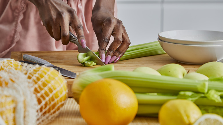 woman cutting celery stalks on wood block