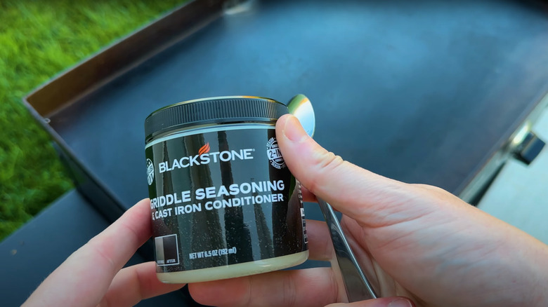 Person holding Blackstone griddle seasoning over clean grill