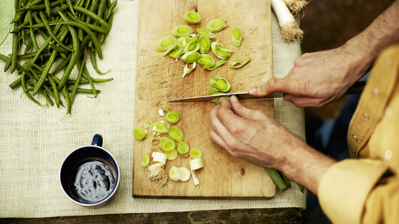 Chopping green onions on a wooden cutting board with greens on the table