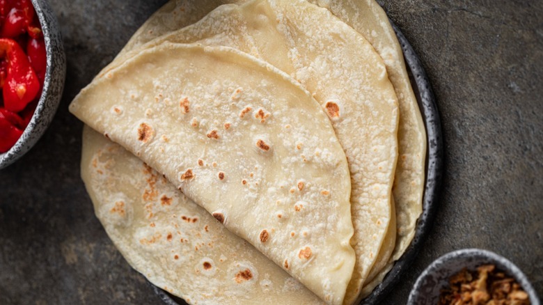 Stack of folded tortillas on big plate on dark surface