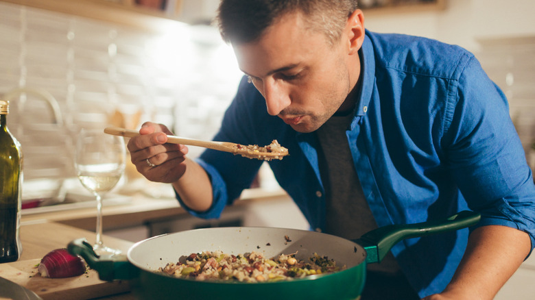 young man tasting risotto from the pot