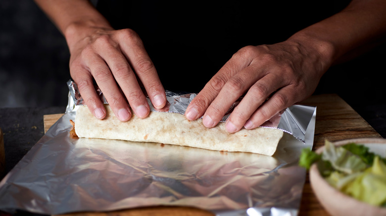 Hands wrap burrito in foil
