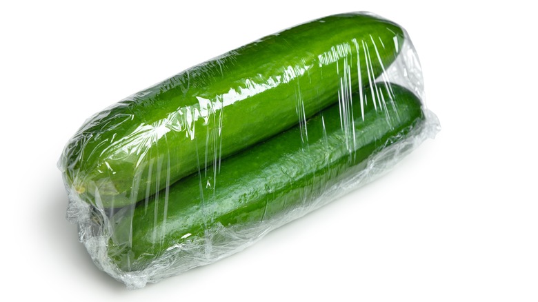 two cucumbers sealed in cling plastic wrap on white background