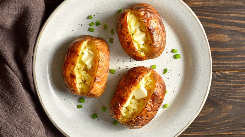 Three hot baked potatoes with butter on a white plate