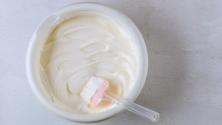 A bowl of white frosting with a pink rubber spatula