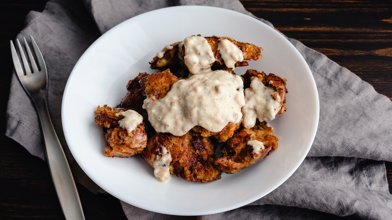 Fried chicken covered in white gravy on a white plate