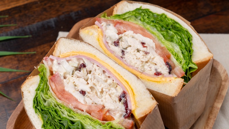 Two halves of a chicken salad sandwich with lettuce and tomato wrapped in brown paper