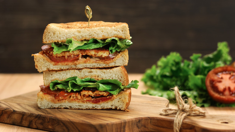 Two halves of a tofu BLT sandwich stacked on a wooden board