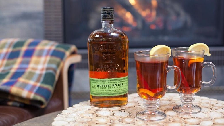 bulleit rye whiskey and cocktail with lemon and fireplace in background