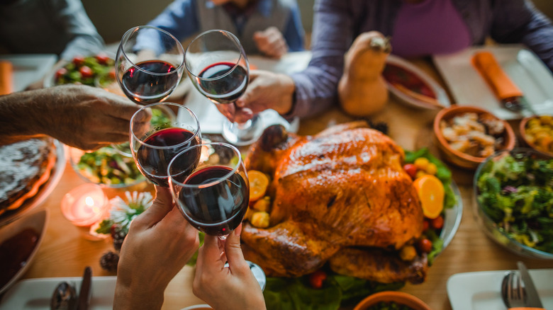 A group of people clink glasses filled with red wine over a Thanksgiving dinner.