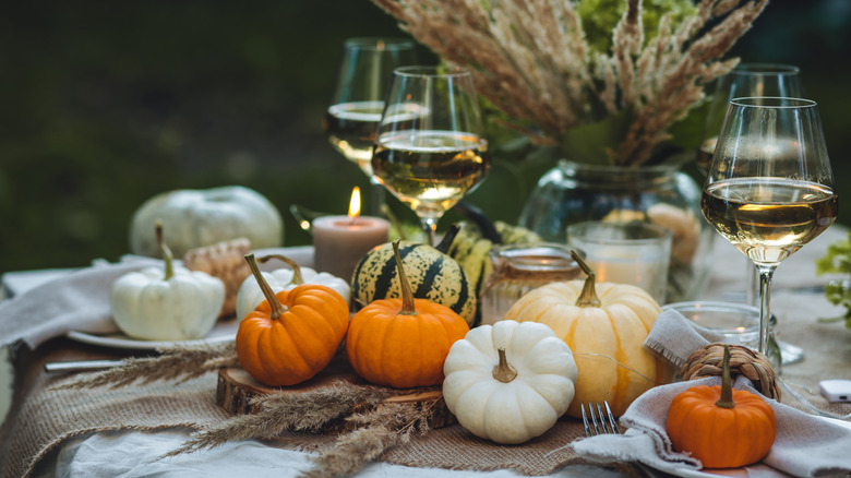 A table decorated with pumpkins, with glasses of wine on it.