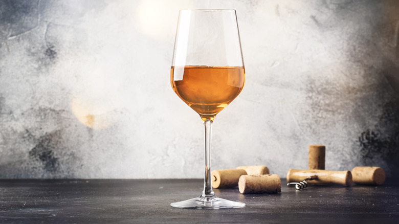 glass of orange wine on wooden table with corks and corkscrew