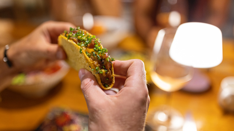 hands holding a hard shell taco with glass of rose in the background