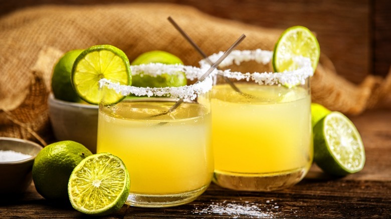 Two margaritas rimmed with salt and limes 