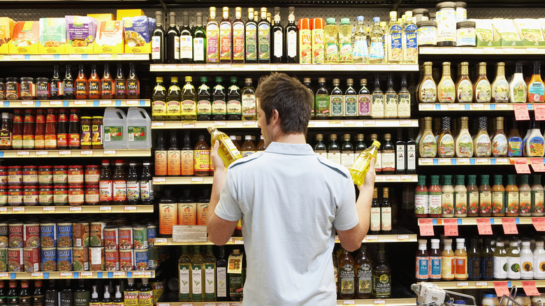 Man comparing bottles of oil in grocery store