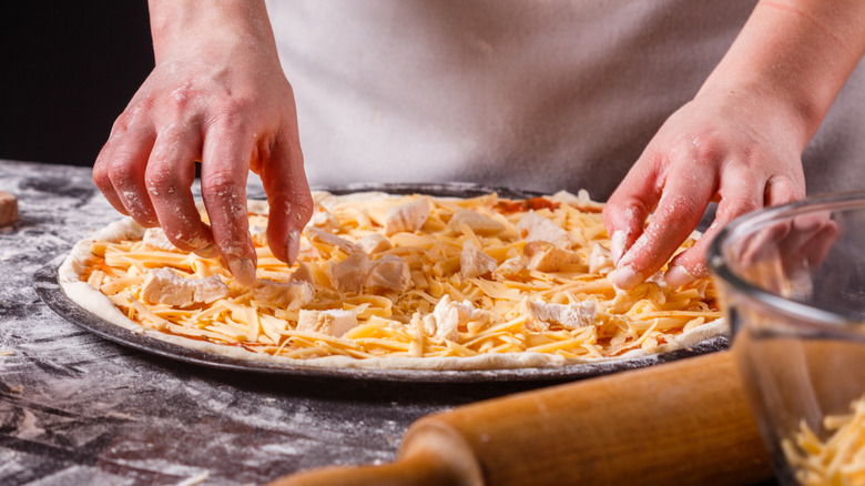 A chef places pieces of chicken onto an uncooked cheese pizza