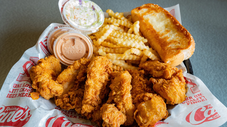 Golden fried chicken fingers with fries, a thick piece of toast, and small plastic cups of coleslaw and light orange sauce on Raising Cane's paper