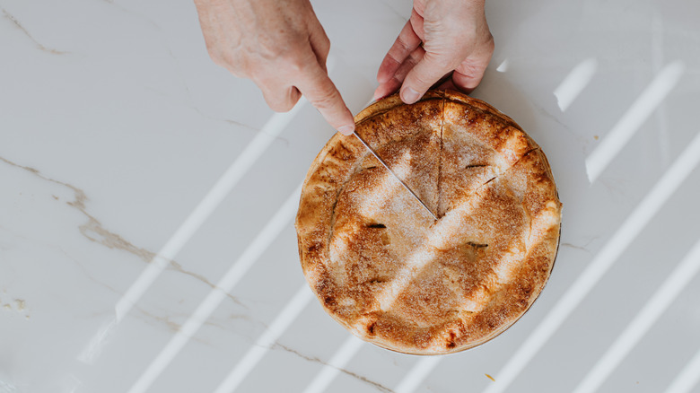 Person using two hands to cut into a freshly baked pie