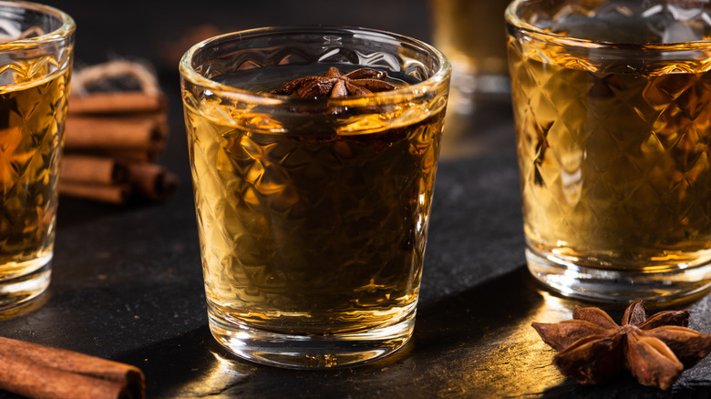 Three short cocktail glasses filled with rum with star anise on top