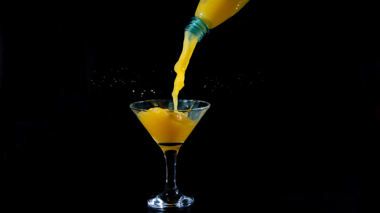 Orange juice being poured from bottle into martini glass