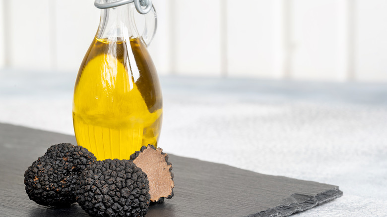 Truffle oil in a glass jar beside truffles on a kitchen slab.