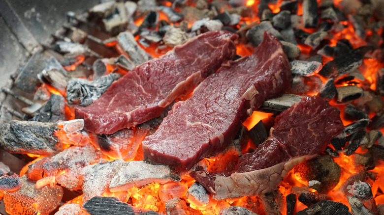 Three steaks cooking on a glowing bed of coals