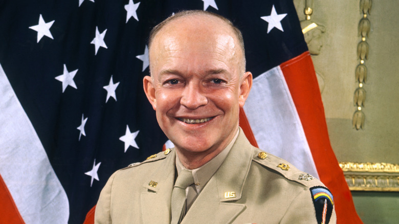 Dwight Eisenhower smiles as he sits before a large American flag