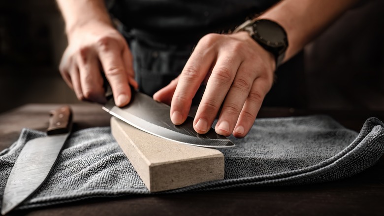 A man sharpens a knife on a whetstone